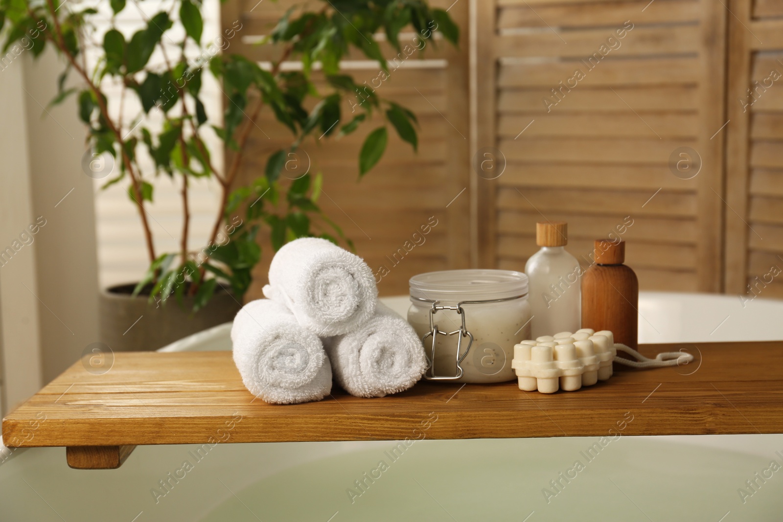 Photo of Wooden tray with spa products and towels on bath tub in bathroom