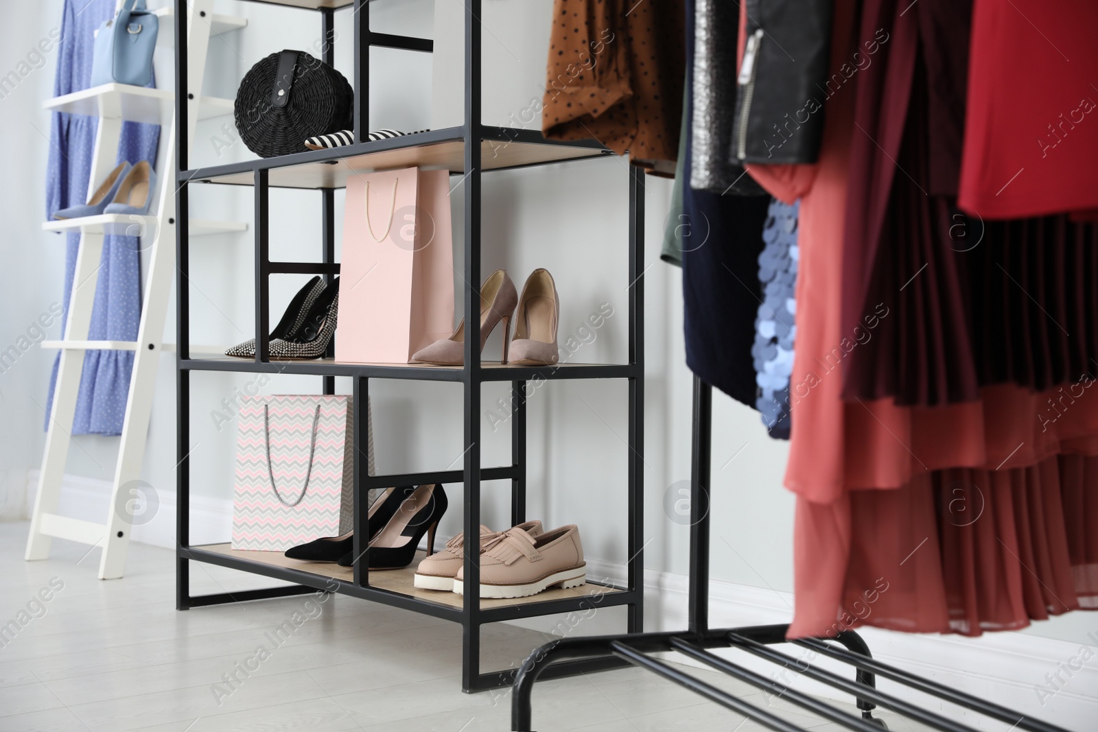 Photo of Different stylish shoes and bags on shelving unit in dressing room