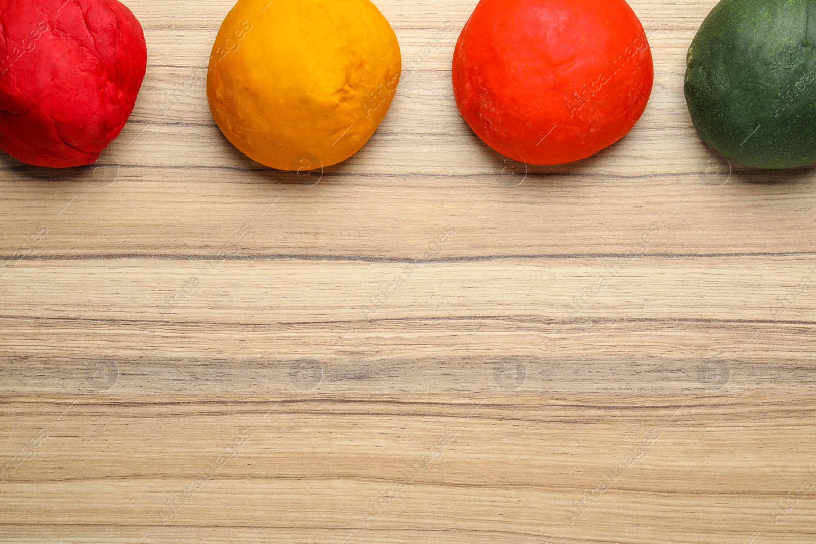 Photo of Dough painted with food colorings on wooden table, flat lay. Space for text