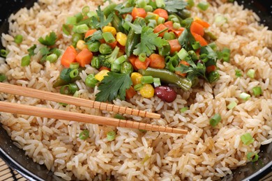 Photo of Tasty fried rice with vegetables and chopsticks in pan, closeup