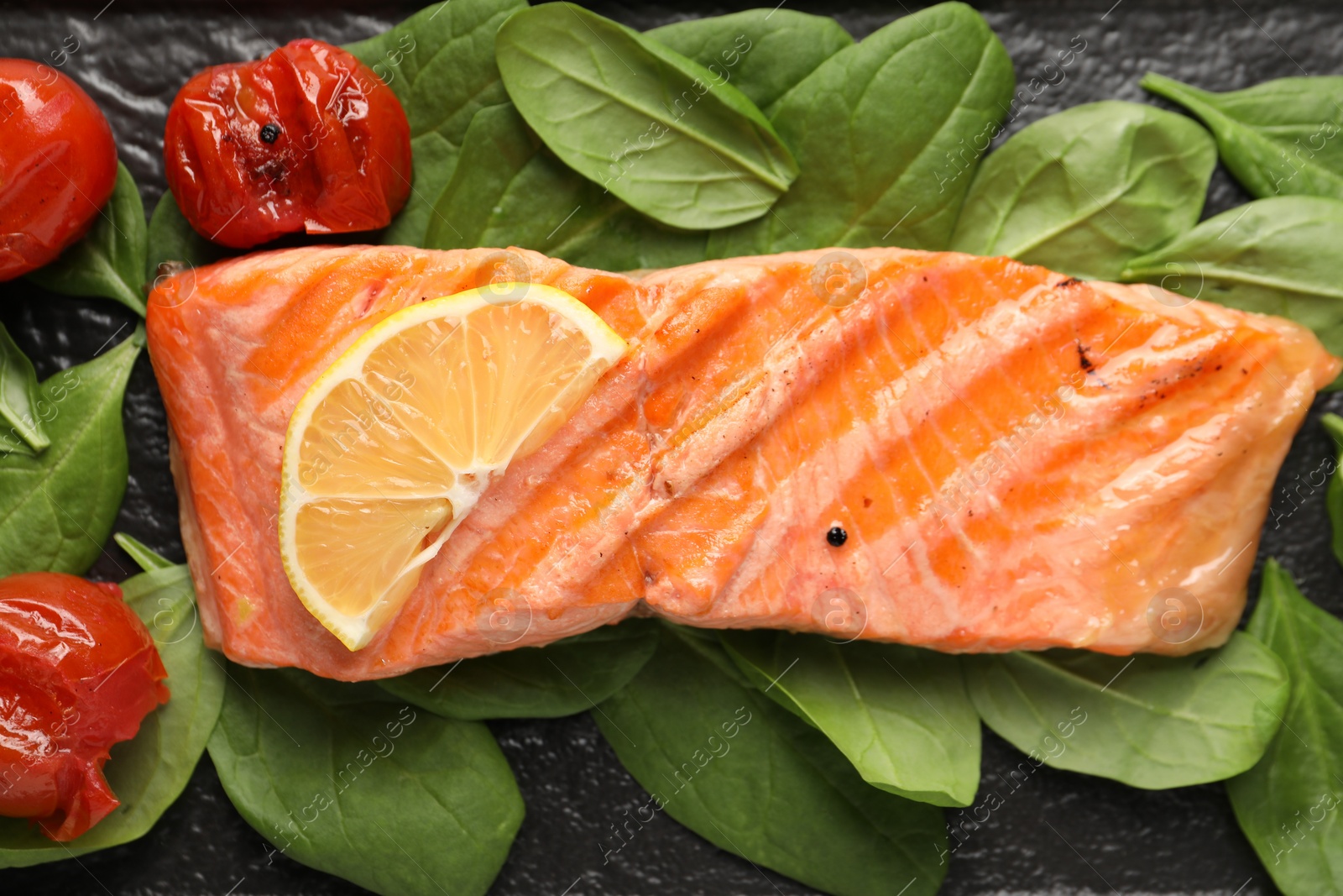 Photo of Tasty grilled salmon with tomatoes, spinach and lemon on table, top view