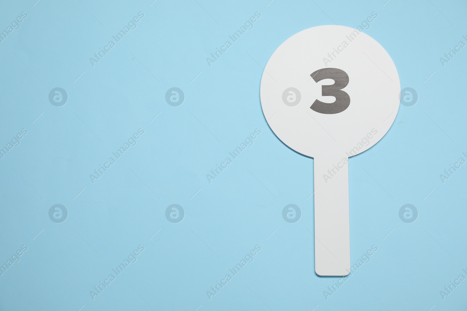 Photo of Auction paddle with number 3 on light blue background, top view. Space for text