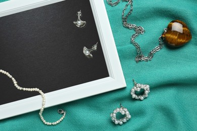 Photo of Beautiful picture and luxury jewelry on turquoise fabric, flat lay