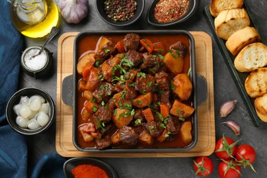 Delicious beef stew and ingredients on grey table, flat lay
