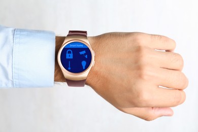Image of Young man showing electronic wristwatch with Smart Home Interface on light background, closeup