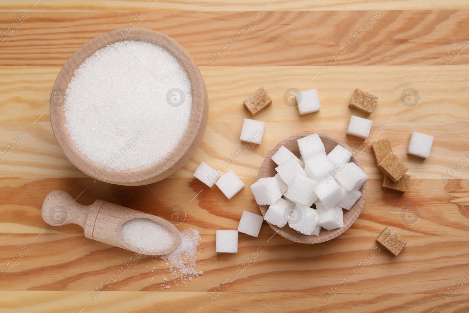 Photo of Bowls and scoop with different types of sugar on wooden table, flat lay