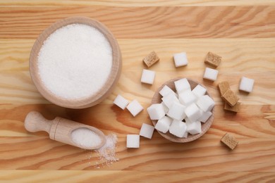 Photo of Bowls and scoop with different types of sugar on wooden table, flat lay