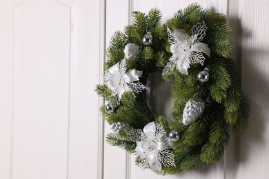 Beautiful Christmas wreath with festive decor hanging on white door, space for text