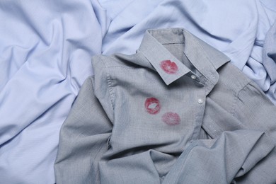 Photo of Men's shirt with lipstick kiss mark among other clothes as background, top view