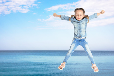 Cute school girl jumping near sea, space for text. Summer holidays