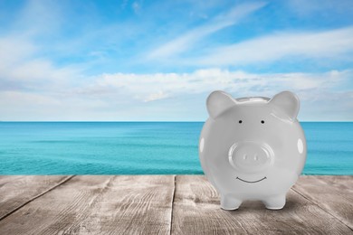 Image of Saving money for summer vacation. Piggy bank on wooden surface near sea, space for text