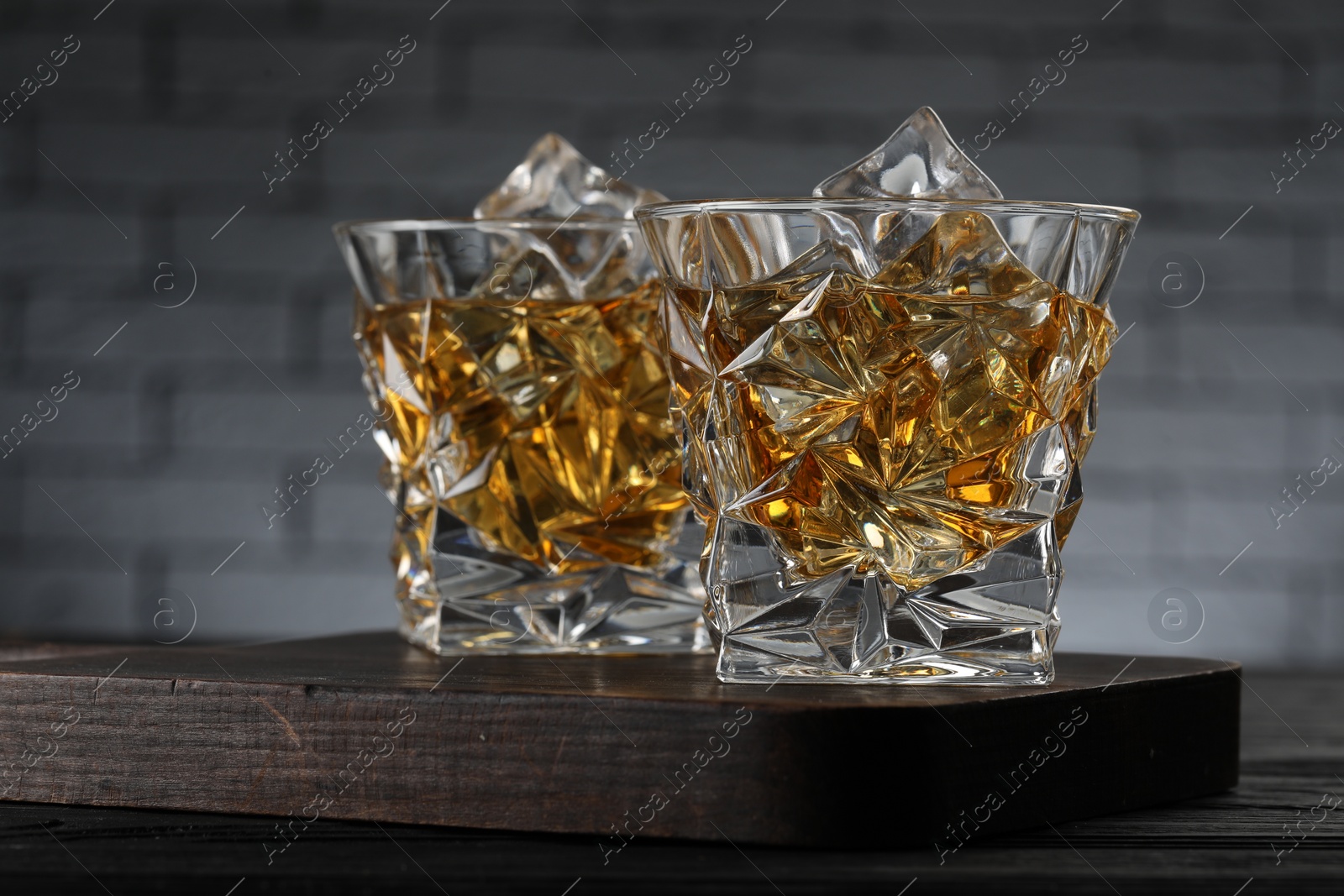 Photo of Whiskey and ice cubes in glasses on black wooden table, closeup