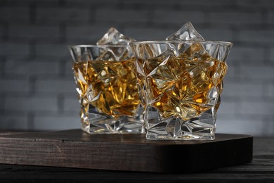 Whiskey and ice cubes in glasses on black wooden table, closeup