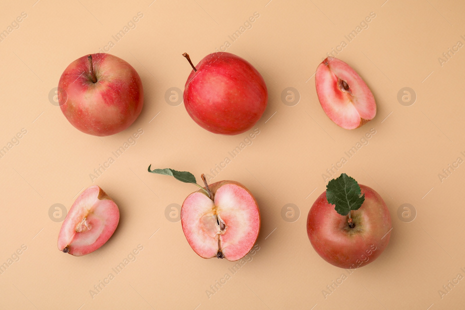 Photo of Tasty apples with red pulp and leaves on beige background, flat lay