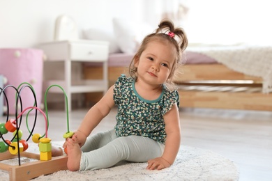 Photo of Adorable little baby girl playing with bead maze on floor in room