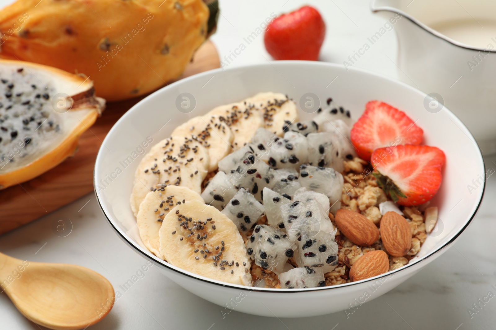 Photo of Bowl of granola with pitahaya, banana and strawberry on white table, closeup