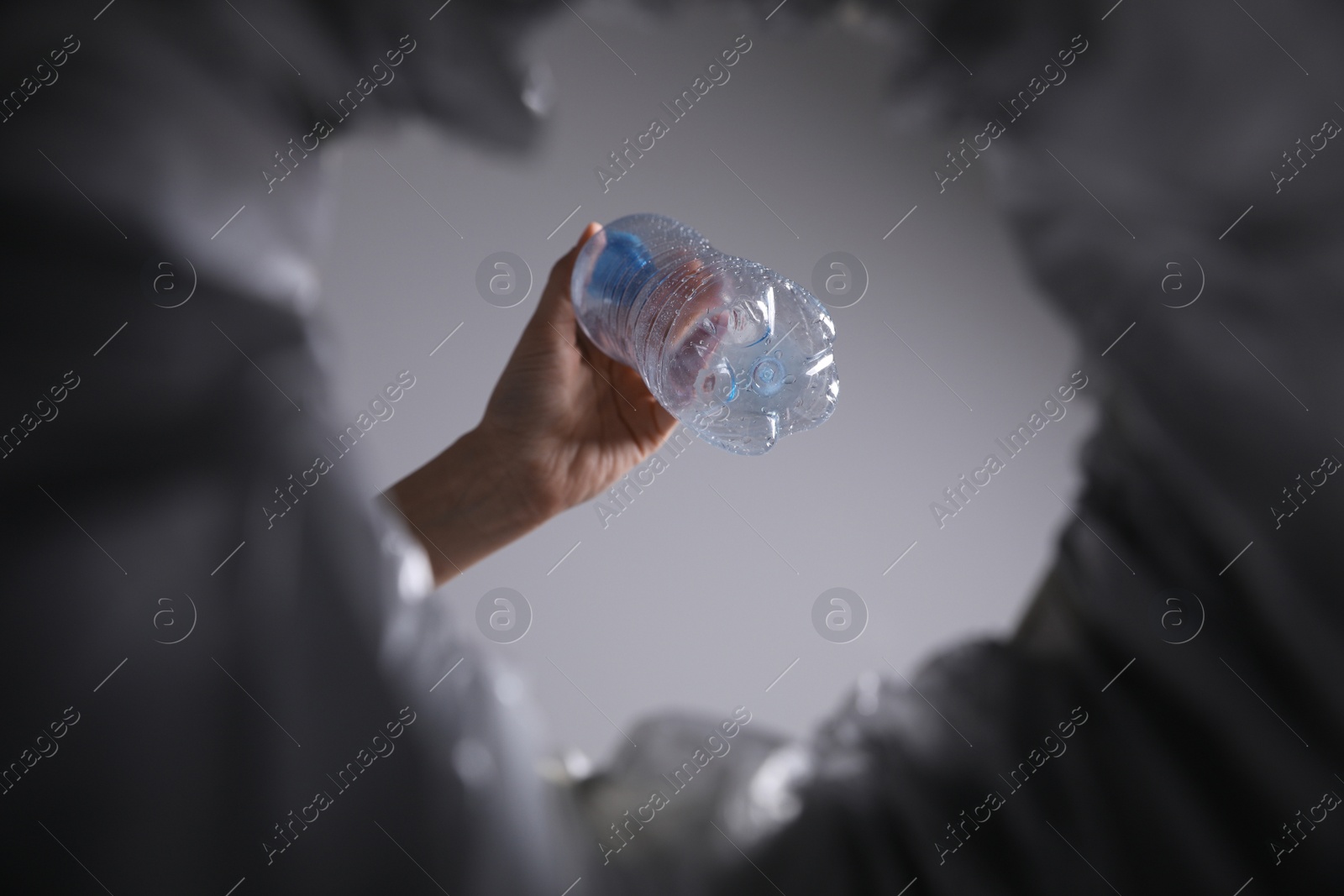 Photo of Bottom view of woman throwing plastic bottle into trash bin on grey background, closeup