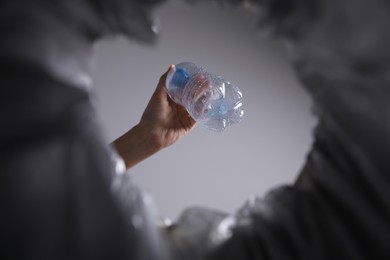 Photo of Bottom view of woman throwing plastic bottle into trash bin on grey background, closeup