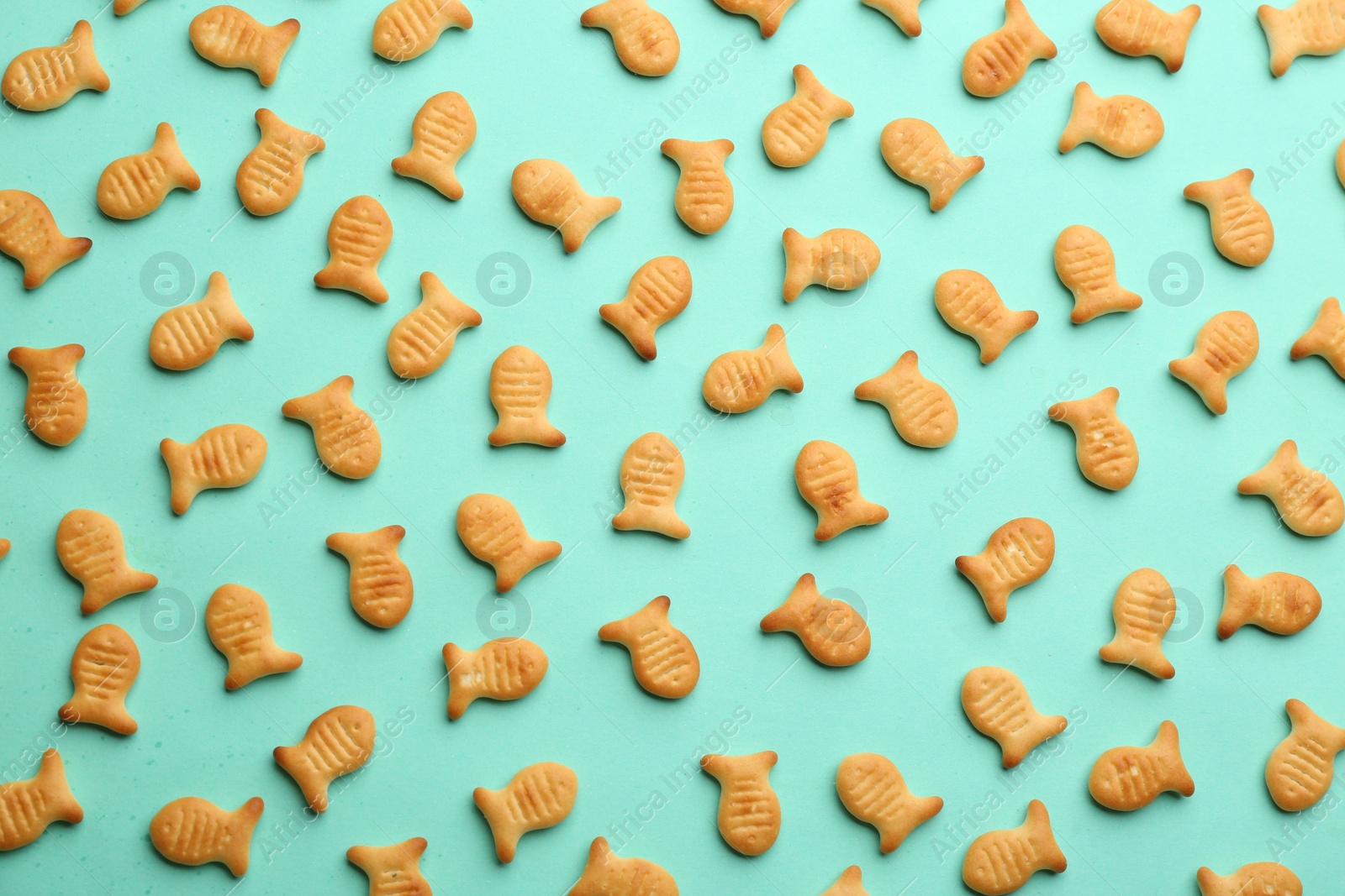 Photo of Delicious goldfish crackers on turquoise background, flat lay