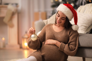 Happy pregnant woman with Christmas ball at home. Expecting baby