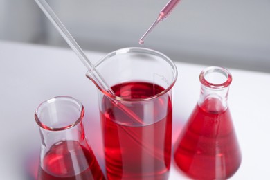 Laboratory analysis. Dripping red liquid into beaker on white table, closeup