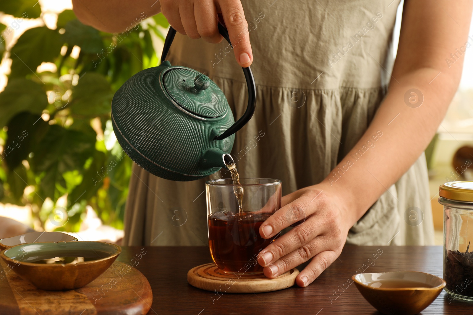 Photo of Woman pouring freshly brewed tea from teapot into cup at wooden table indoors, closeup. Traditional ceremony