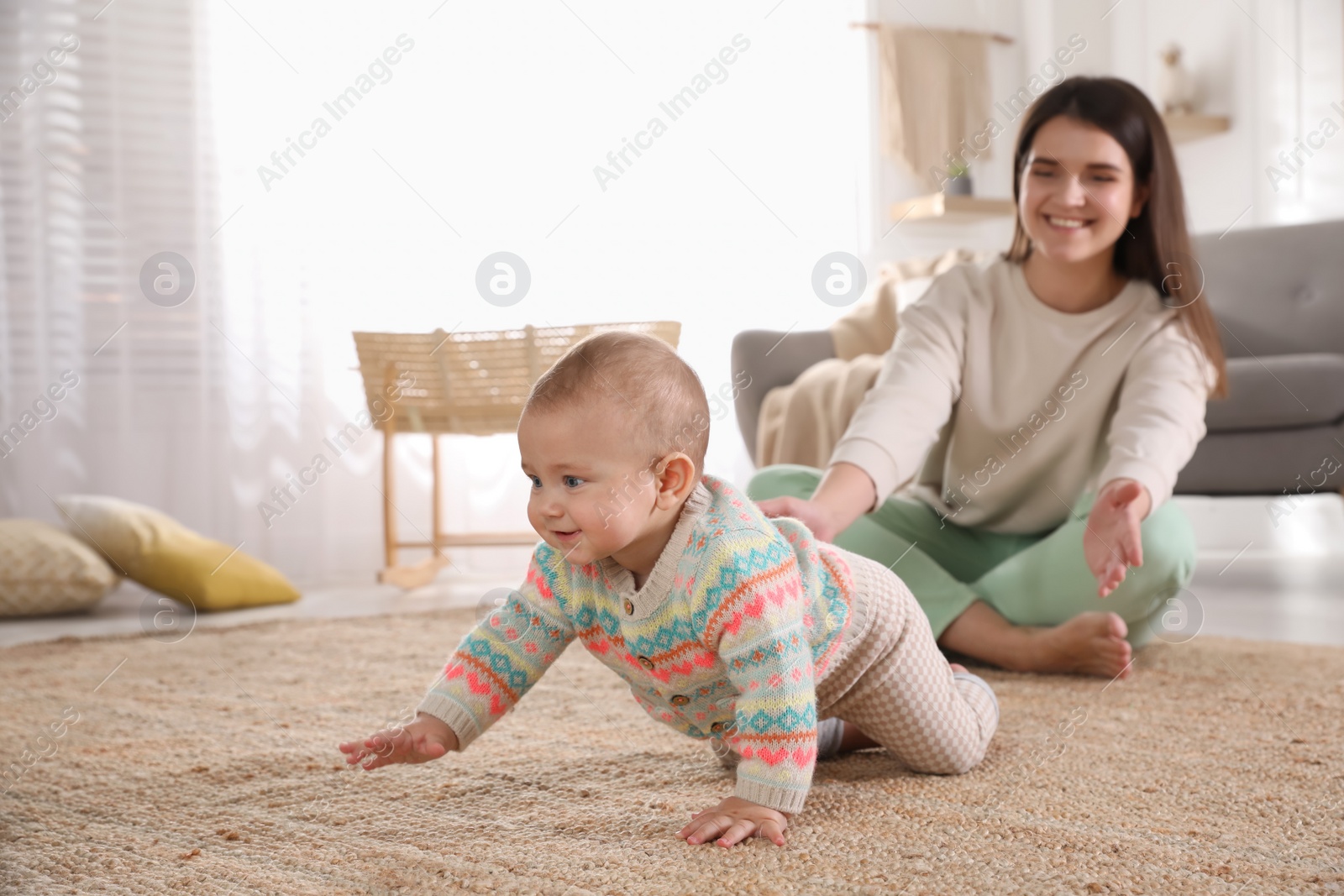 Photo of Happy young mother watching her cute baby crawl on floor at home