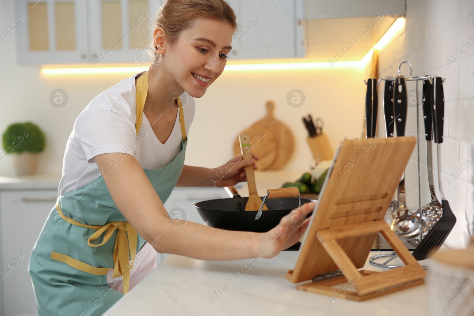 Photo of Young woman with tablet cooking on stove in kitchen