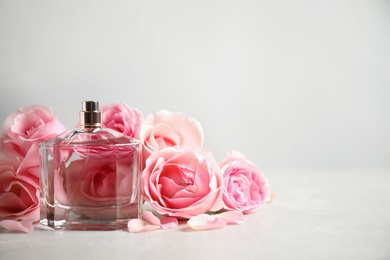 Photo of Bottle of perfume and beautiful roses on light table. Space for text