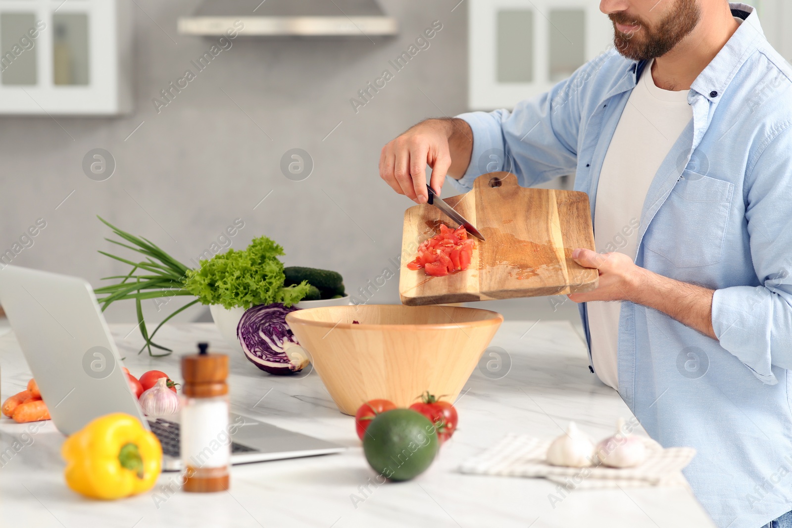 Photo of Man making dinner while watching online cooking course via laptop in kitchen, closeup