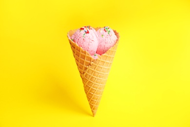 Photo of Delicious ice cream in wafer cone on yellow background