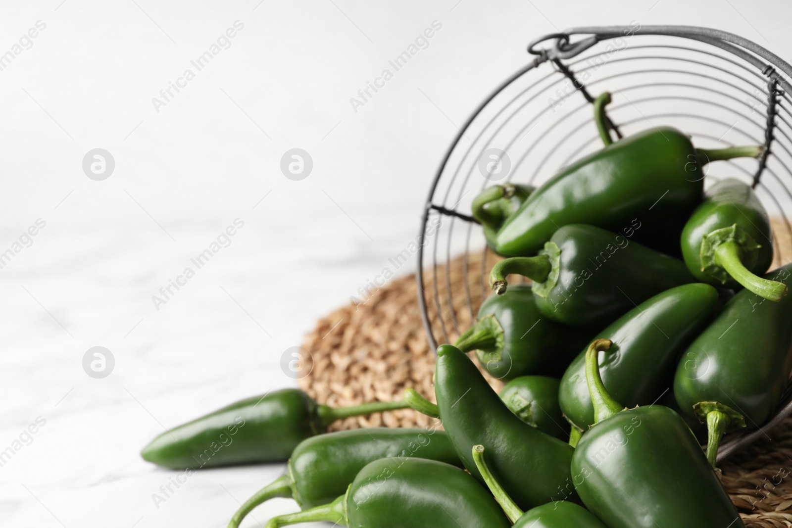 Photo of Green chili peppers and metal basket on marble table. Space for text