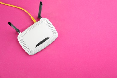 Photo of Modern Wi-Fi router on pink background, top view. Space for text