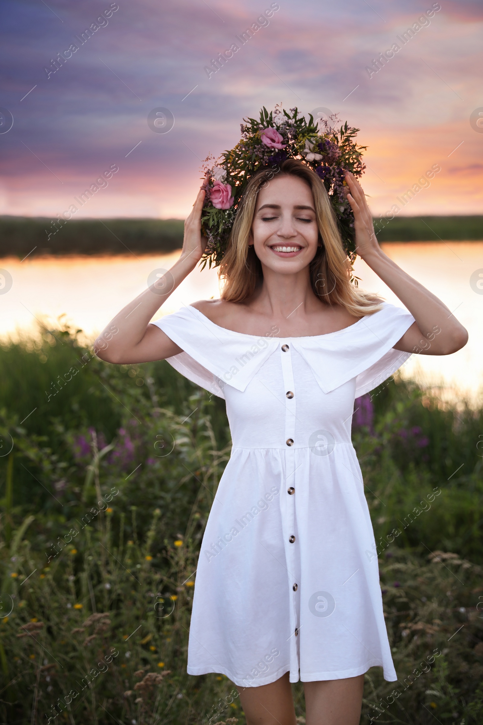 Photo of Young woman wearing wreath made of beautiful flowers outdoors at sunset