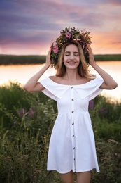 Young woman wearing wreath made of beautiful flowers outdoors at sunset