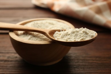 Photo of Baking powder in bowl and spoon on wooden table, closeup