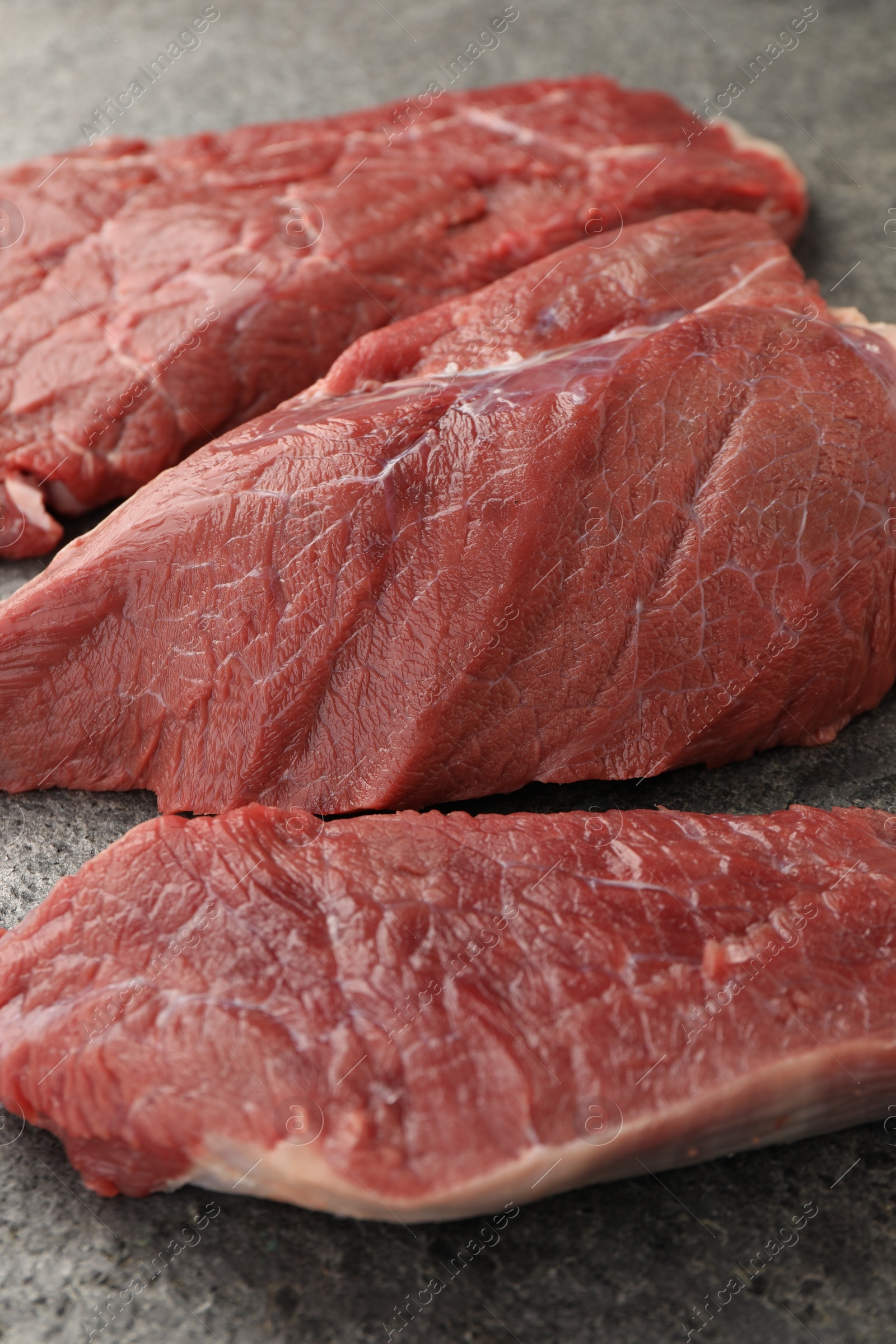 Photo of Pieces of raw beef meat on grey table, closeup