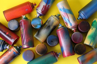 Photo of Many spray paint cans with caps on yellow background, flat lay