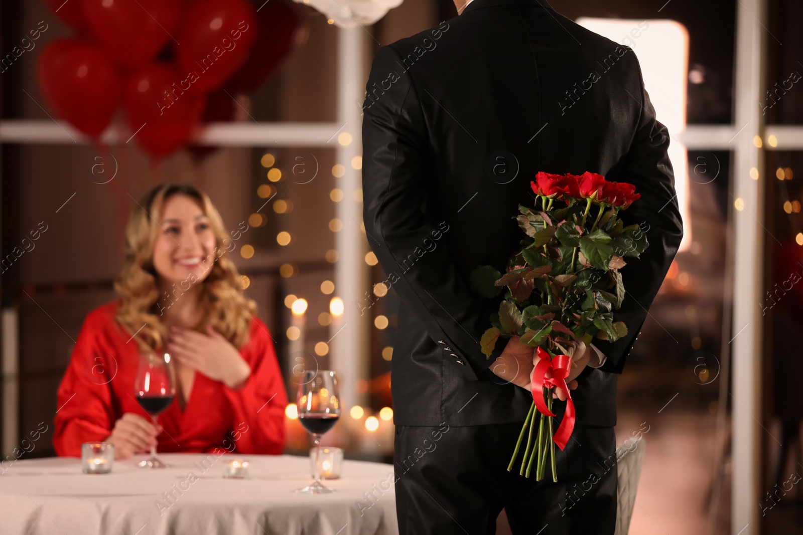 Photo of Man hiding roses for his beloved woman in restaurant at Valentine's day dinner