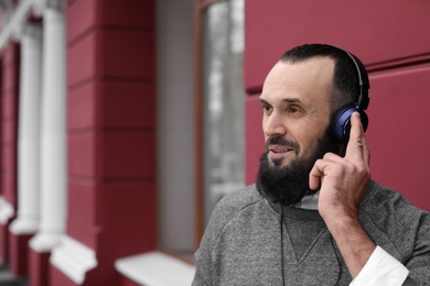 Photo of Mature man with headphones listening to music outdoors. Space for text