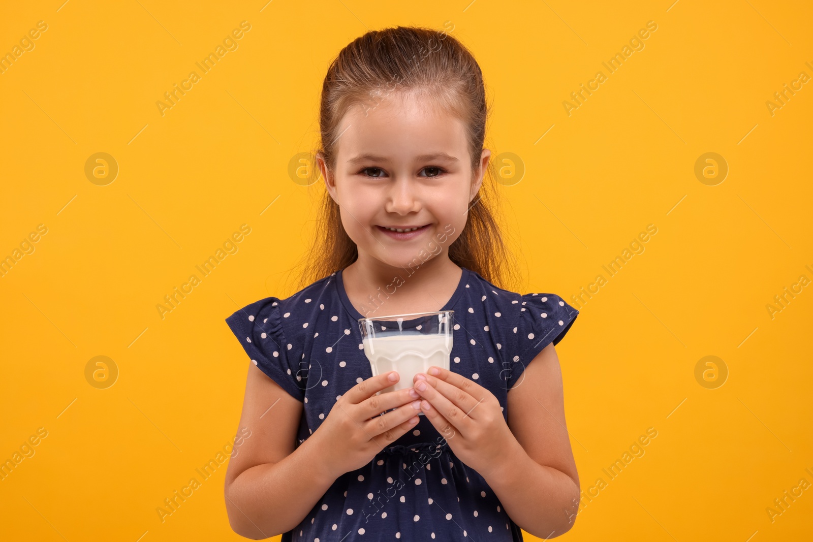 Photo of Cute girl with glass of fresh milk on orange background