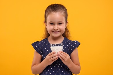 Photo of Cute girl with glass of fresh milk on orange background