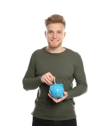 Young man putting money into piggy bank on white background