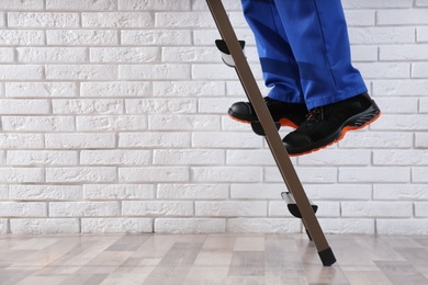 Professional worker climbing up ladder indoors, closeup. Space for text