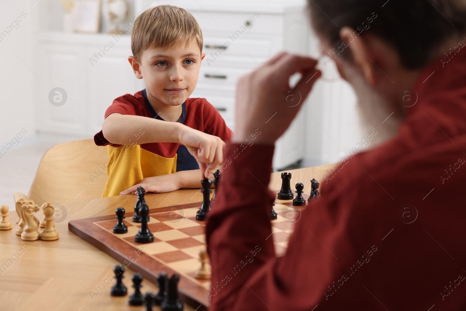 Photo of Little boy playing chess with his grandfather at table in room