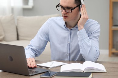 Photo of E-learning. Young man using laptop during online lesson at table indoors.