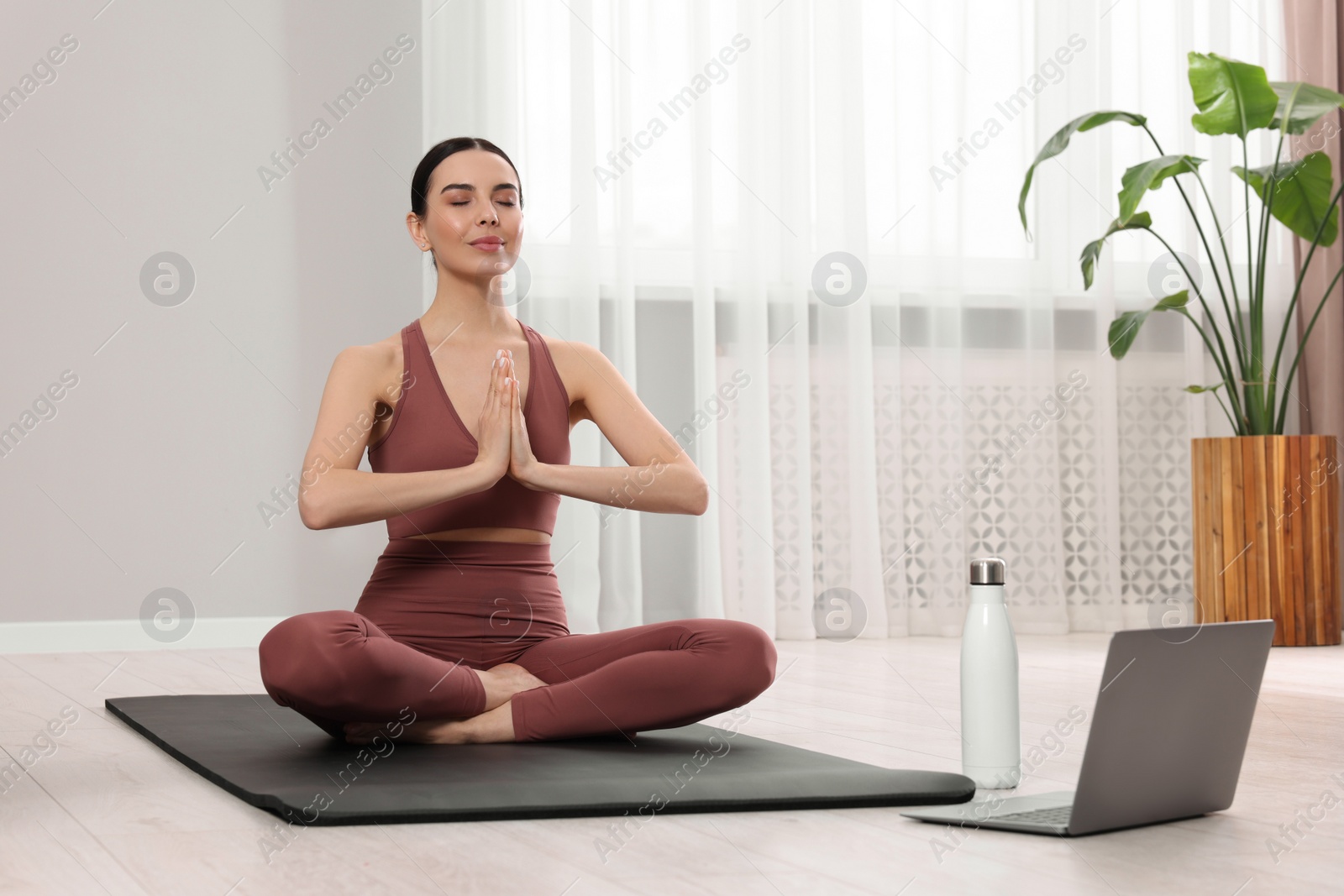 Photo of Woman in sportswear meditating near laptop at home, space for text