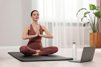 Photo of Woman in sportswear meditating near laptop at home, space for text