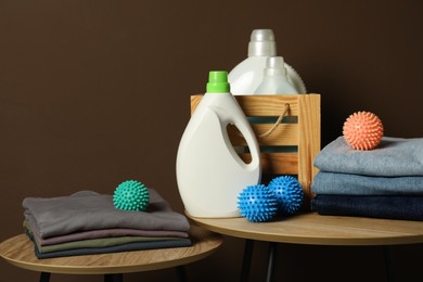Photo of Many dryer balls, stacked clean clothes and laundry detergents on wooden tables