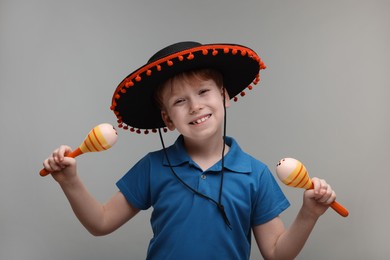 Cute boy in Mexican sombrero hat with maracas on grey background